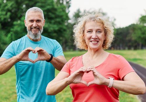 Older couple making a heart shape with their hands outdoors after a heart health check