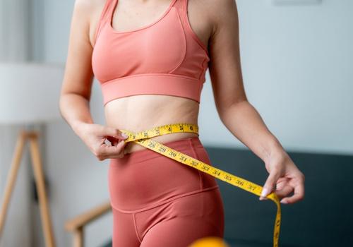Woman measuring her waist with a tape measure as part of a weight loss program