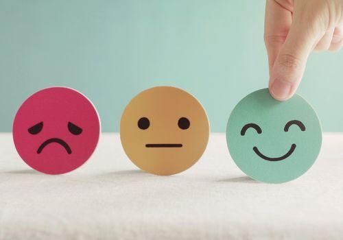 Hand pointing to a smiling face among sad, neutral and happy face cards