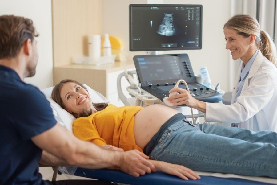Smiling pregnant woman having a pregnancy ultrasound scan with her partner beside her as a female clinician checks the baby on screen