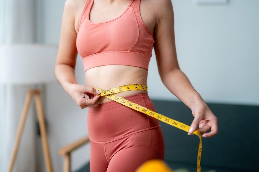 Woman in activewear measuring her waist with a yellow tape measure as part of a GP weight management check